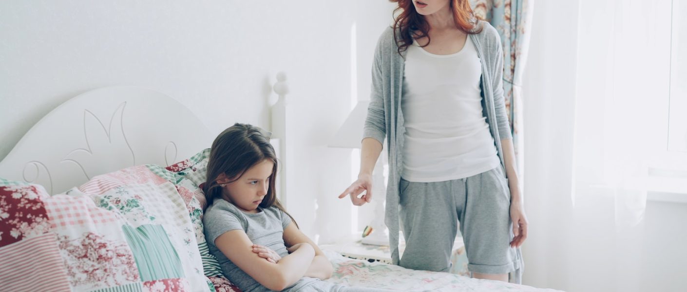 Mother scolds her daughter, who is sitting on the bed.