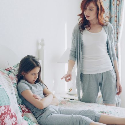 Mother scolds her daughter, who is sitting on the bed.